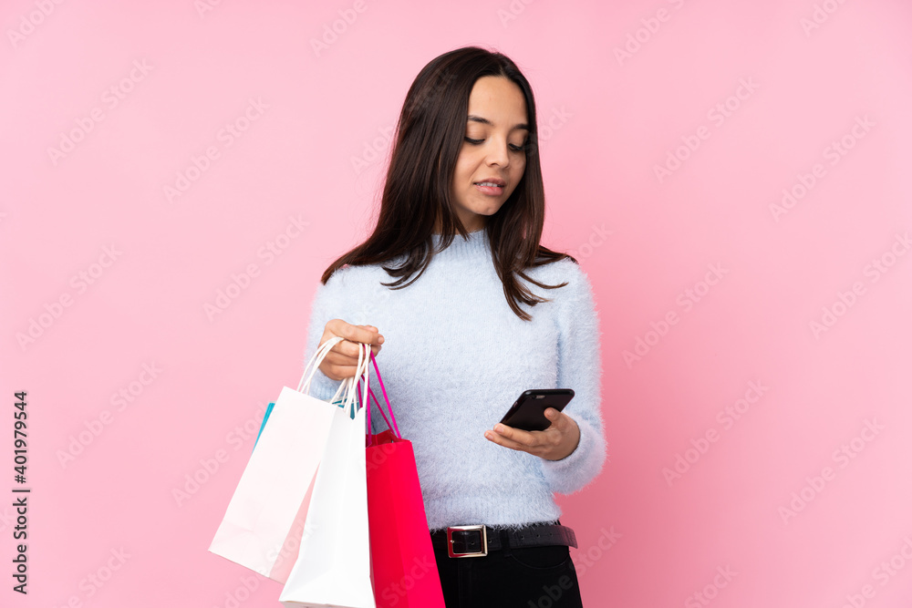 Young woman with shopping bag over isolated pink background holding coffee to take away and a mobile