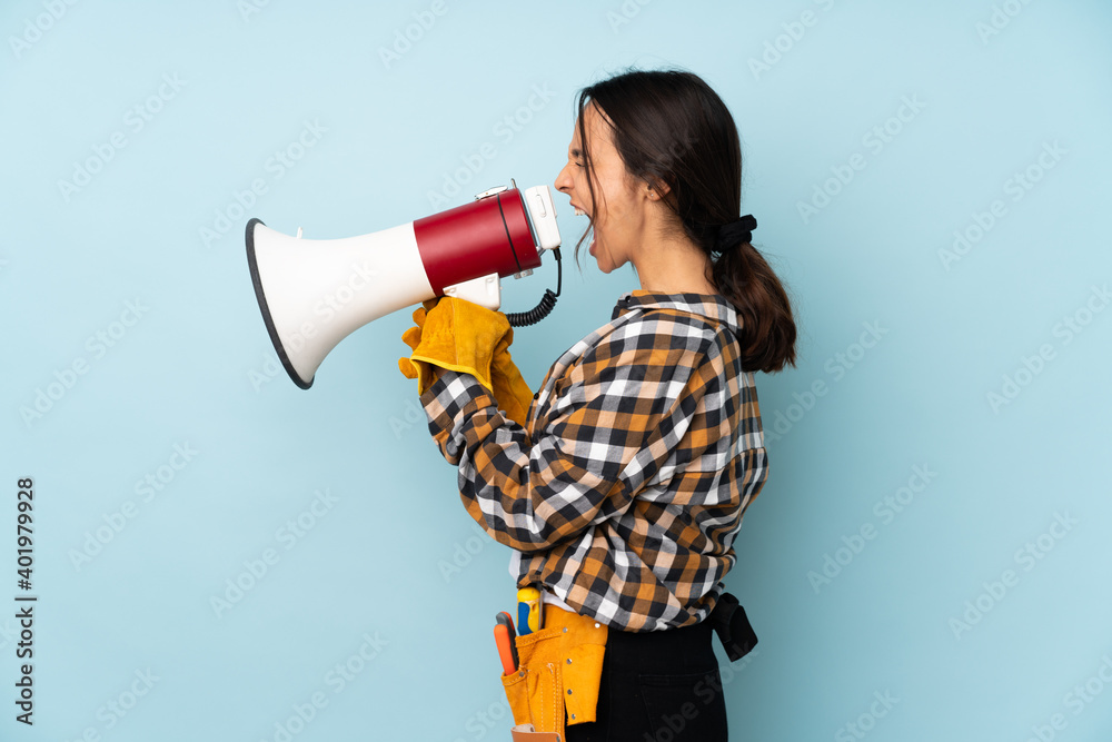 Young electrician woman isolated on blue background shouting through a megaphone Young electrician woman isolated on blue background shouting through a megaphone