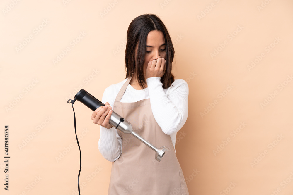 Young brunette girl using hand blender over isolated background having doubts Young brunette girl using hand blender over isolated background having doubts