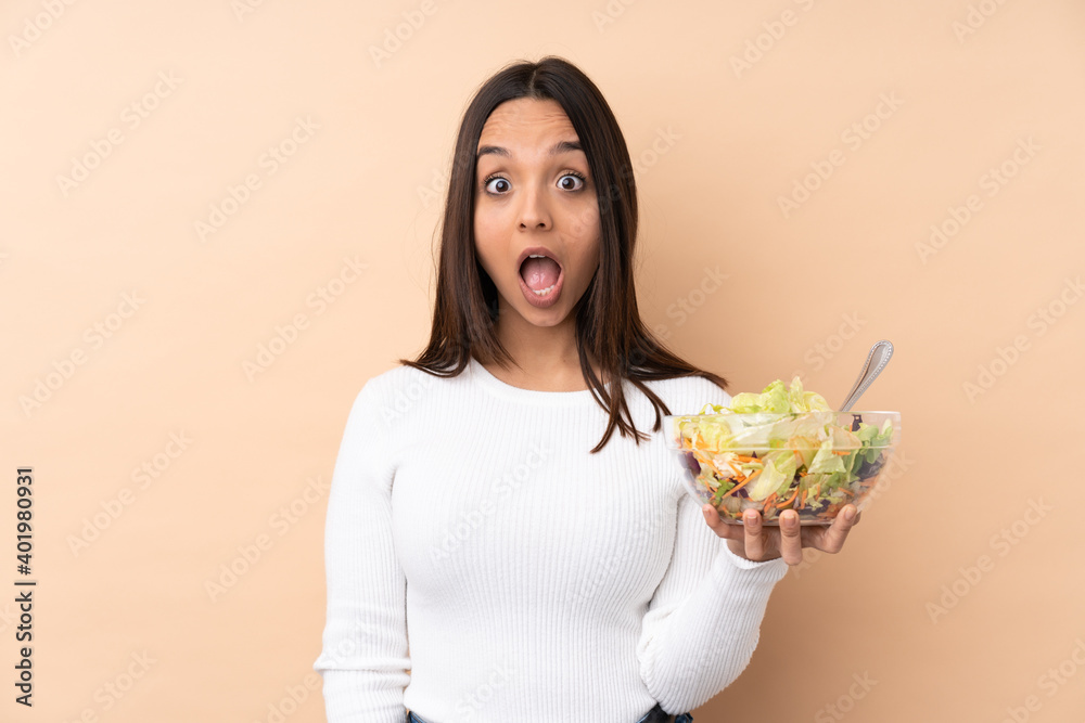 Young brunette girl holding a salad over isolated background with surprise facial expression