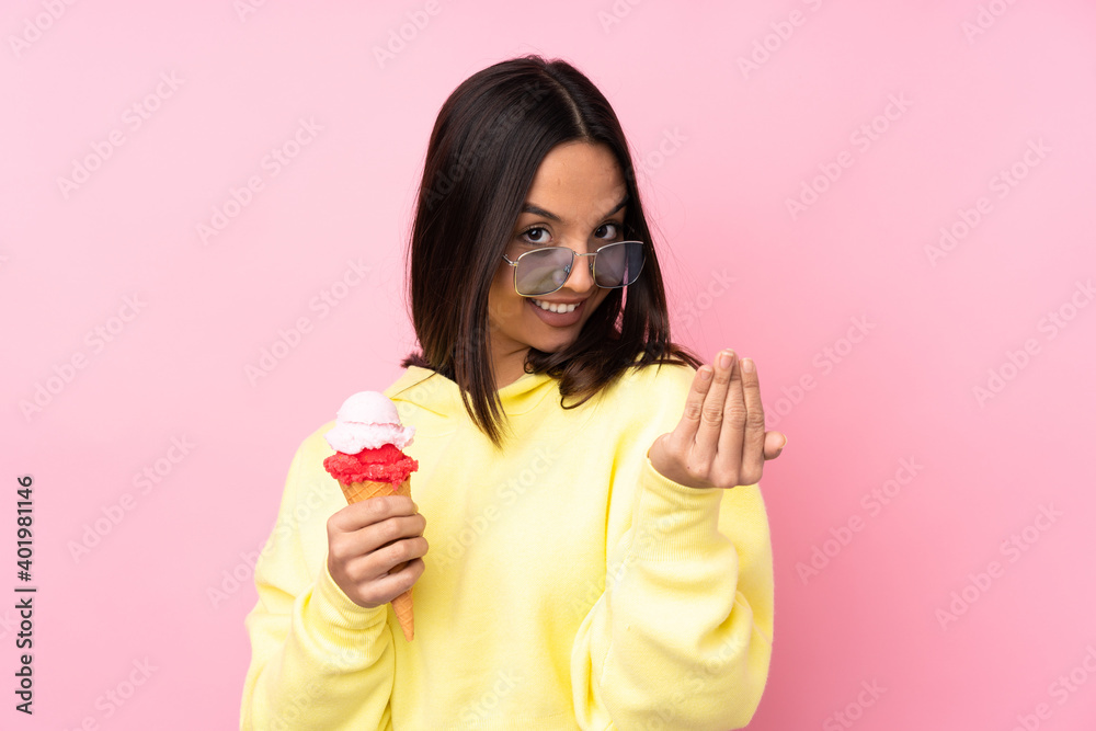 Young brunette girl holding a cornet ice cream over isolated pink background inviting to come with hand. Happy that you came Young brunette girl holding a cornet ice cream over isolated pink background inviting to come with hand. Happy that you came
