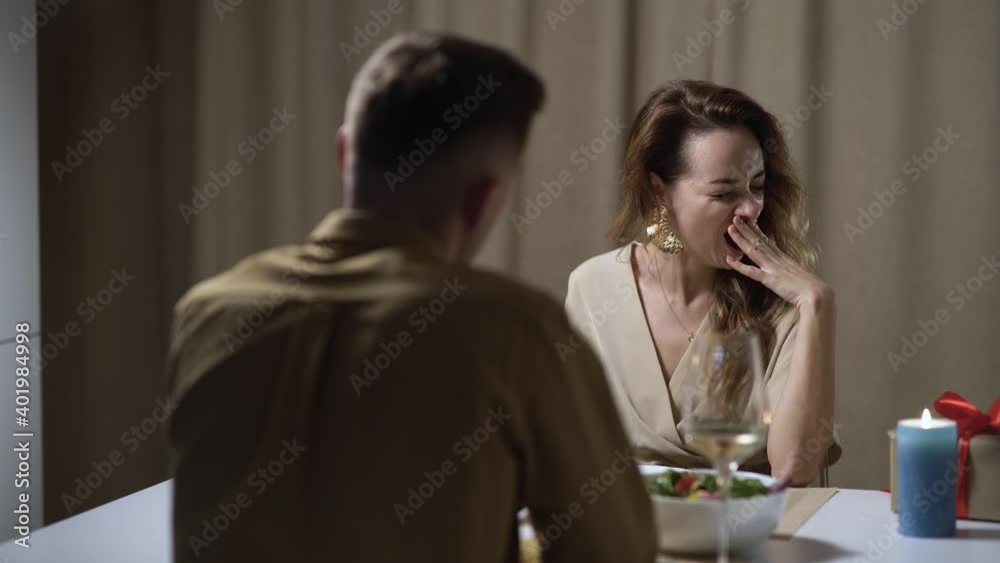 A bored woman yawns while sitting at a table while on a date with a man. The concept is not a good romantic evening.