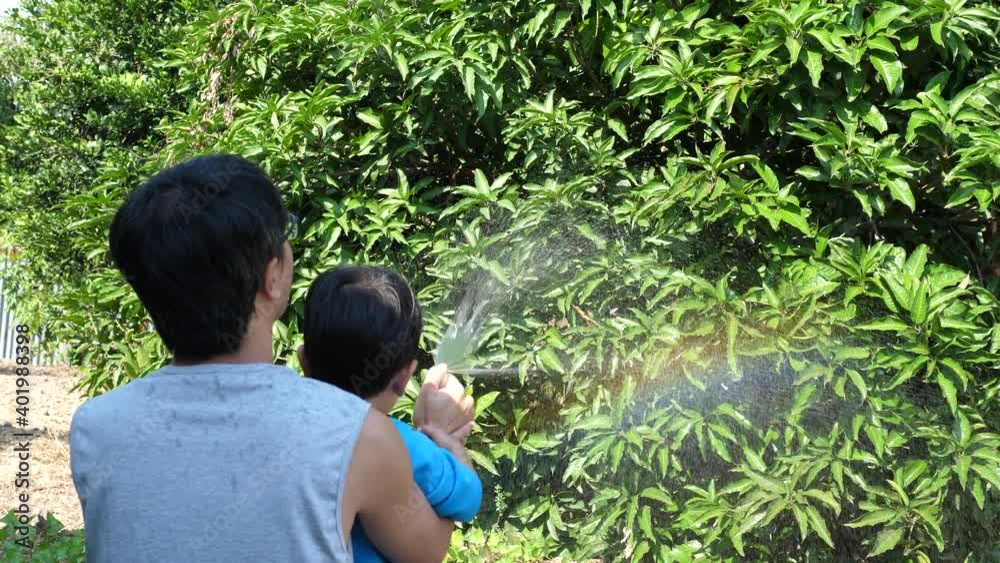 4K Authentic asian child boy and father making beautiful rainbow by water and sunlight together outdoor in garden nature background. Concept of learning nature, fun family activity, good relationship.