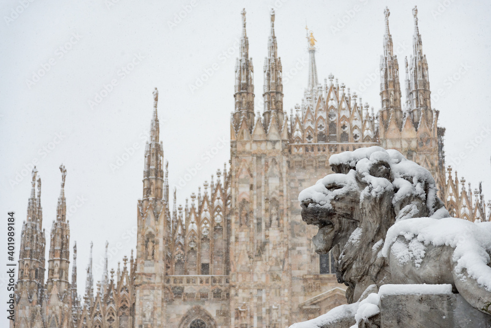 Naklejka premium The facade of the famous Milan Cathedral under a heavy snowfall. Lion statue in the foreground.