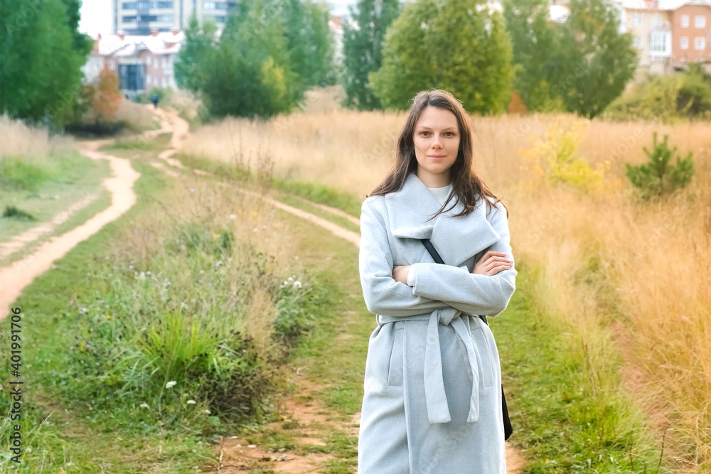 Portrait of young brunette woman in autumn park in city, she is looking at camera and smiling. Wearing in wool gray coat. Walking in park outdoors. Portrait of young brunette woman in autumn park in city, she is looking at camera and smiling. Wearing in wool gray coat. Walking in park outdoors.