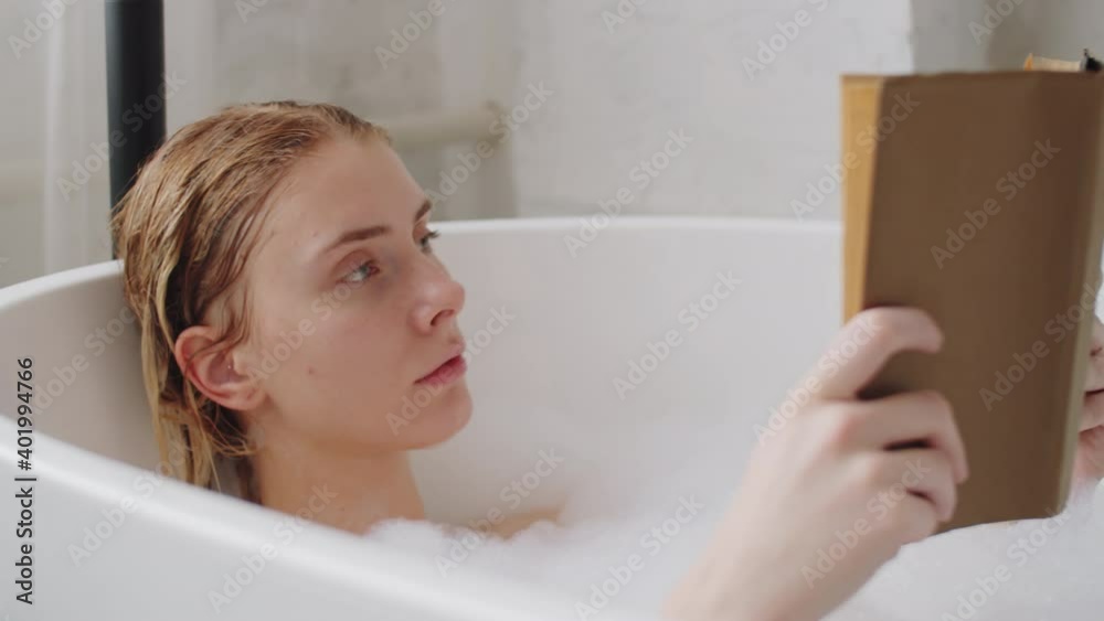 Young attractive Caucasian woman with blonde hair reading a book while taking a bath at home Young attractive Caucasian woman with blonde hair reading a book while taking a bath at home