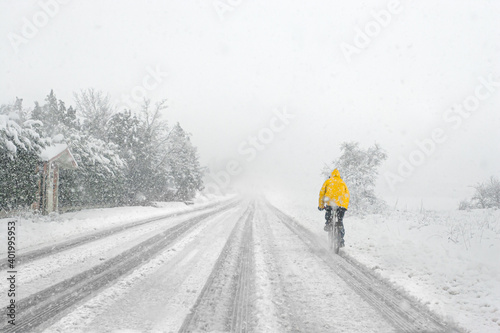 Man riding a bike with yellow jacket on snowy road during a snow storm