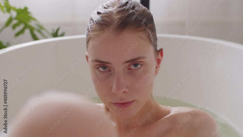 Close up portrait shot of young attractive caucasian woman lying in bath water, then getting out of it and looking at camera seductively Close up portrait shot of young attractive caucasian woman lying in bath water, then getting out of it and looking at camera seductively