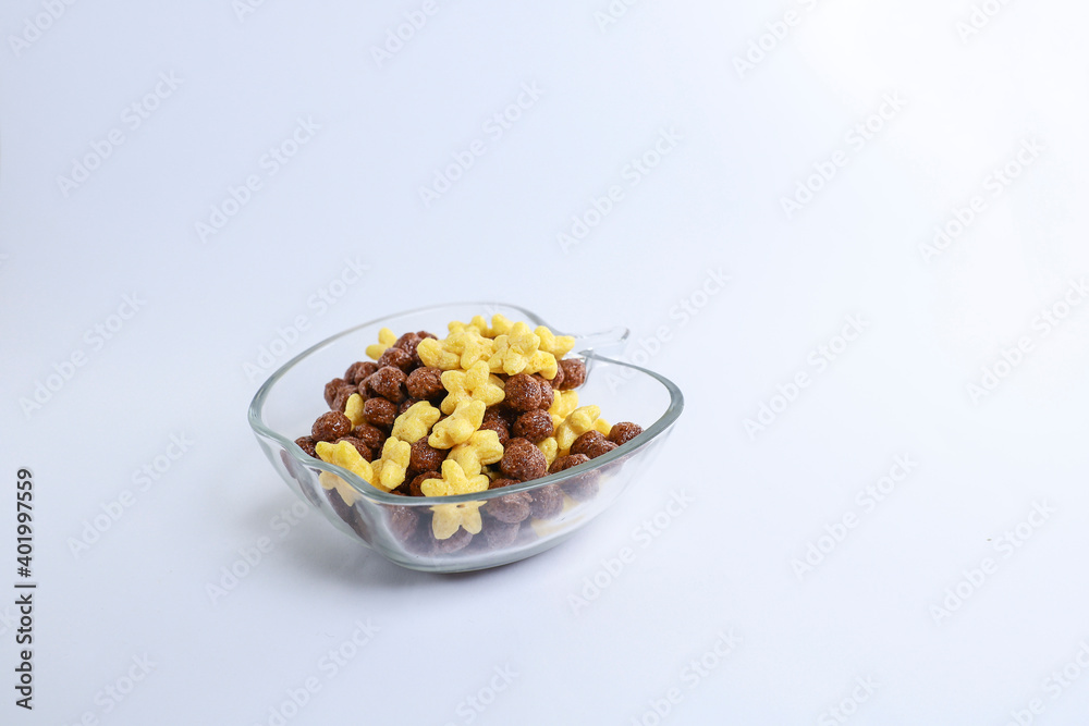 A glass bowl filled with chocolate and corn cereal isolated on the yellow background A glass bowl filled with chocolate and corn cereal isolated on the yellow background