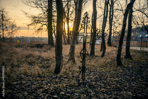Fototapeta Naklejka Na Ścianę i Meble -  Stary krzyż na cmentarzu z zachodzącym słońcem w tle