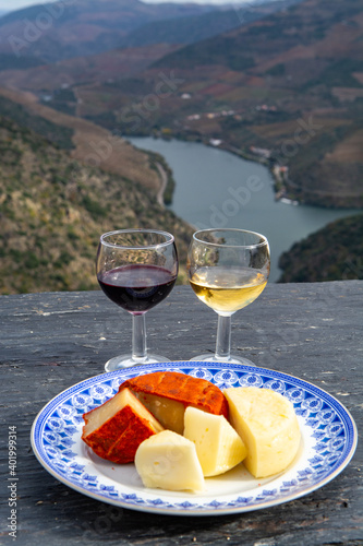 Taste of Portugal, variety of fortified port wines and goat and sheep cheeses, produced in Douro Valley with Douro river and colorful terraced vineyards on background in autumn, Portugal