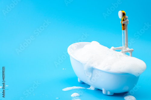 Personal care, relaxing spa pampering and calming bubble bath concept with colourful minimalist image of luxurious bathtub filled with soap suds isolated on blue background with copy space