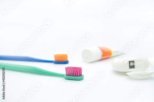 Two colored toothbrushes with bright bristles on the left and a tube of paste and dental floss on the right on a white background  daily oral care