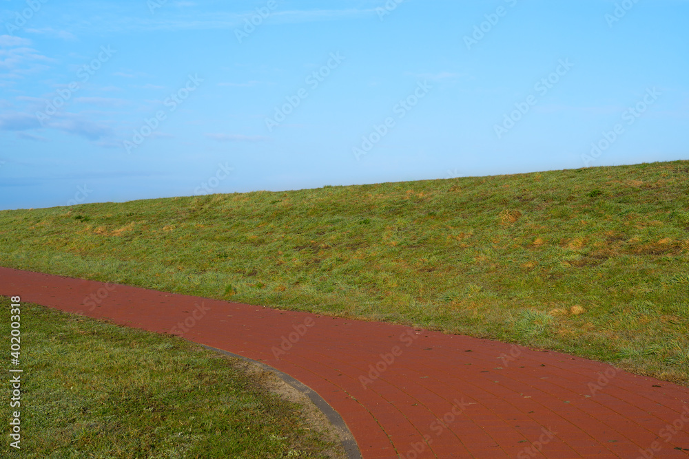 Red Cycling path between the green grassland and a blue sky above it