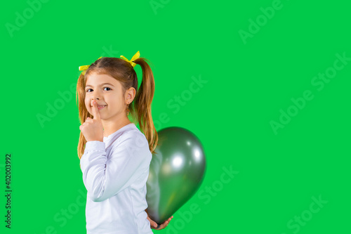 Preschool girl hides a ultimate grey color balloon showing quietly tsss to the camera. Green background and side space. photo