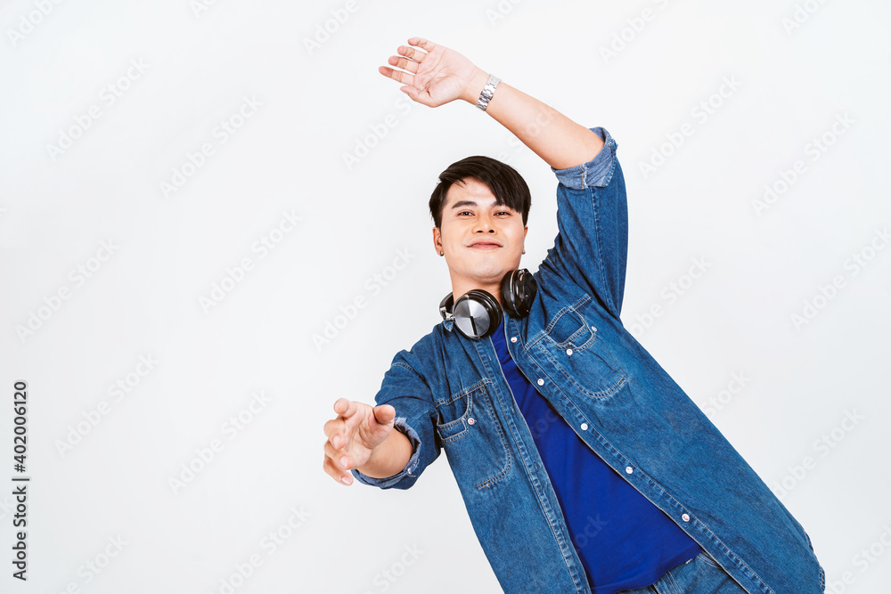 Asian black hair man in a t-shirt with jeans jacket dancing while wearing headphones and music inspired face expression in white background. Asian black hair man in a t-shirt with jeans jacket dancing while wearing headphones and music inspired face expression in white background.