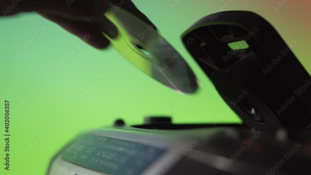 A man takes out a laser CD disk from an old music player on a green background. Hand close up. Retro technique. Previous generation of audio systems