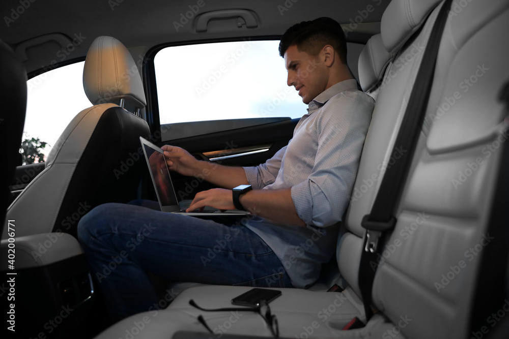 Handsome man working with laptop on backseat of modern car Handsome man working with laptop on backseat of modern car