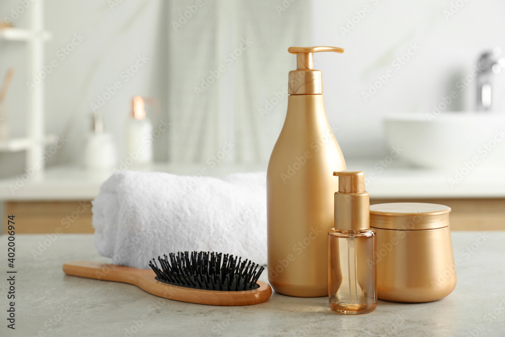 Different hair care products, towel and brush on table in bathroom