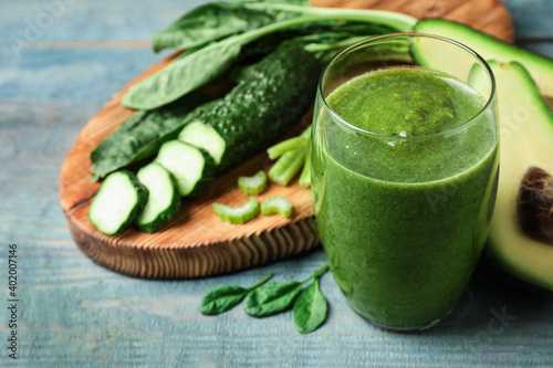 Delicious green juice and fresh ingredients on light blue wooden table, closeup. Space for text