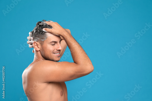 Handsome man washing hair on light blue background, space for text