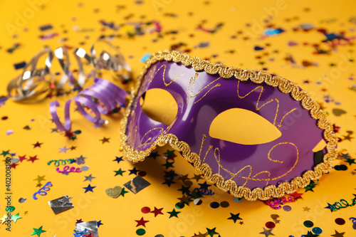 Fototapeta Naklejka Na Ścianę i Meble -  Beautiful purple carnival mask and confetti on yellow background, closeup