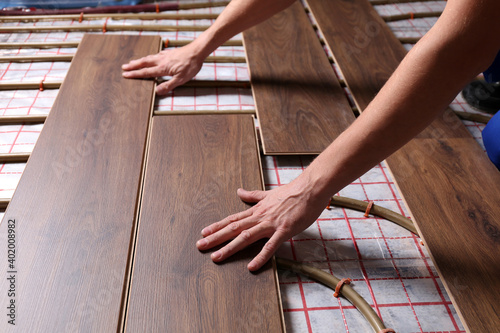 Fotografija Worker installing new wooden laminate over underfloor heating system, closeup