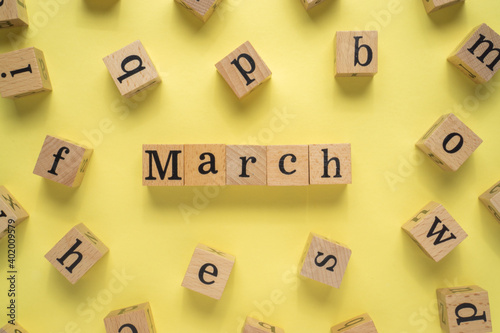 Text MARCH on wooden cubes with a yellow background. Flat lay view concept.