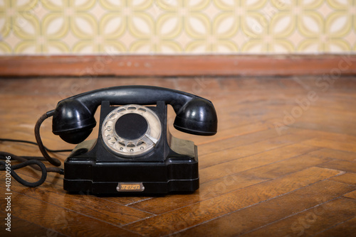Фотография Retro black telephone is on the parquet floor against vintage wallpaper, detail