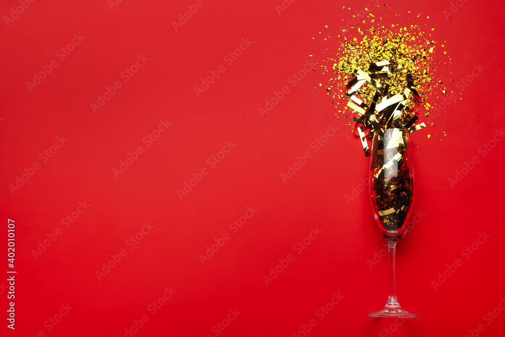 Flat lay composition with confetti and champagne glass on red background. Space for text