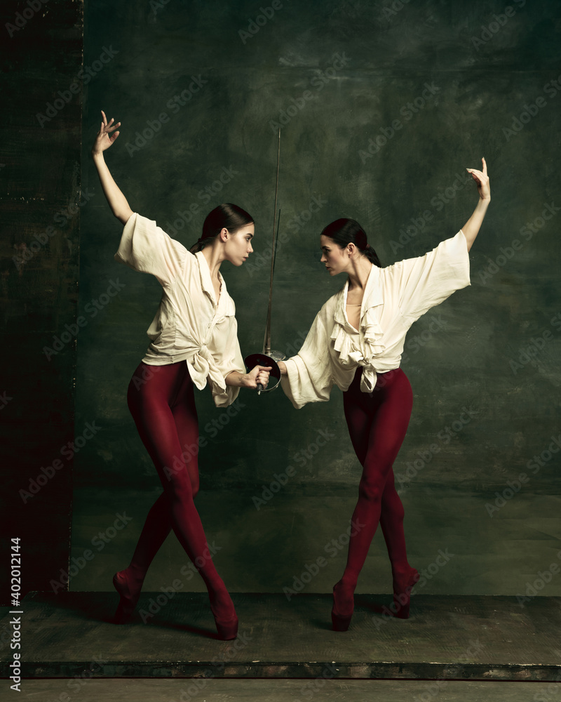Emotions. Two young female ballet dancers like duelists with swords on dark green background. Caucasian models dancing together. Ballet and contemporary choreography concept. Creative art photo.