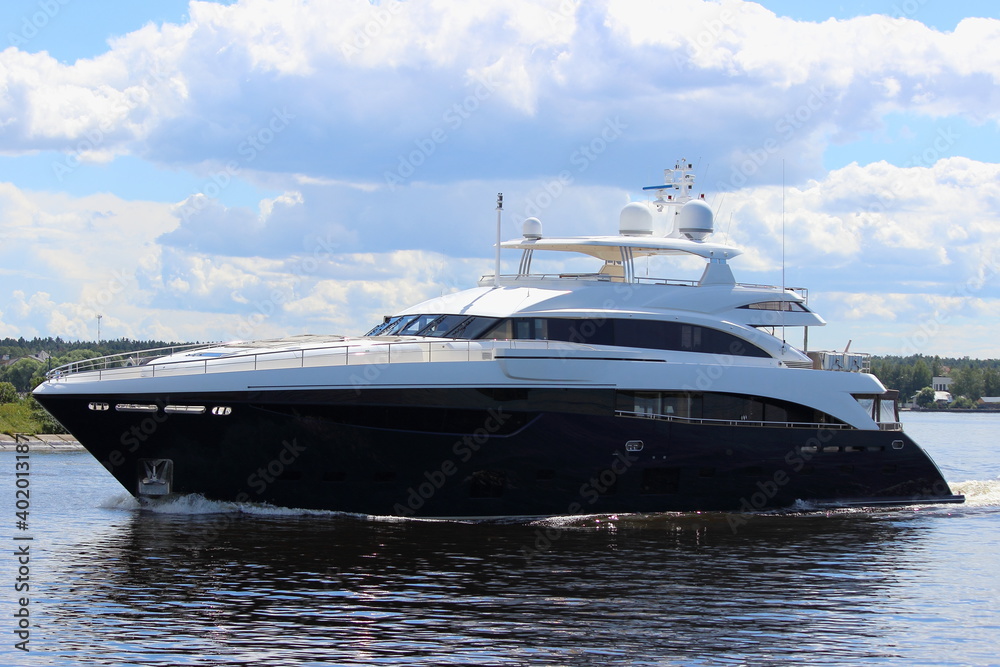 A beautiful pricey large Luxury motor boat slow floats on calm water on blue sky with clouds and green forest on horizon background at Sunny summer day closeup side view, VIP recreation on river A beautiful pricey large Luxury motor boat slow floats on calm water on blue sky with clouds and green forest on horizon background at Sunny summer day closeup side view, VIP recreation on river