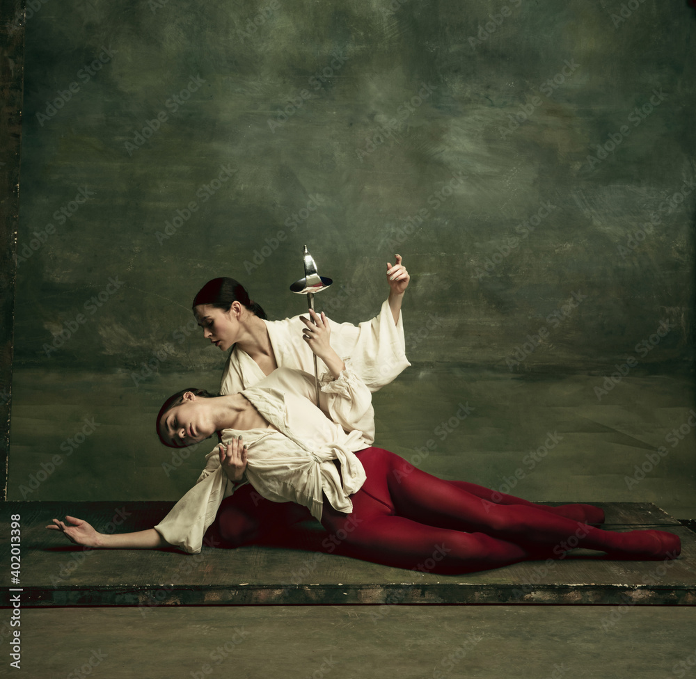 Moment. Two young female ballet dancers like duelists with swords on dark green background. Caucasian models dancing together. Ballet and contemporary choreography concept. Creative art photo.