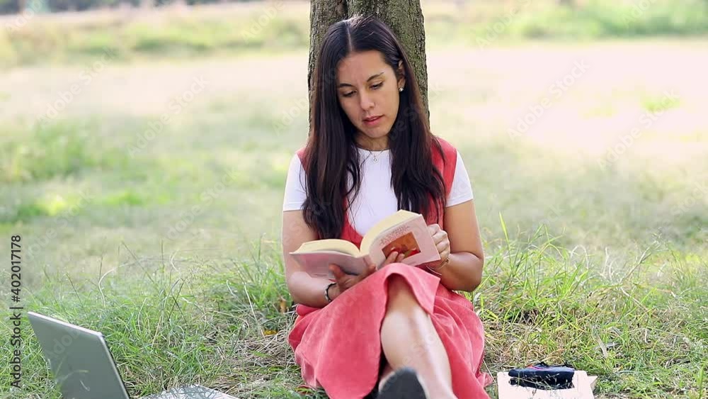 Acercamiento a rostro de Mujer latina leyendo un libro en el parque, sentada en el césped recargada de un árbol.	