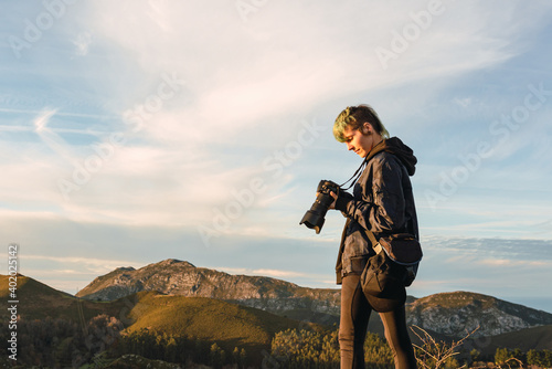 Young professional photographer with punk style reviewing his pictures on a work day at sunset in the mountains.