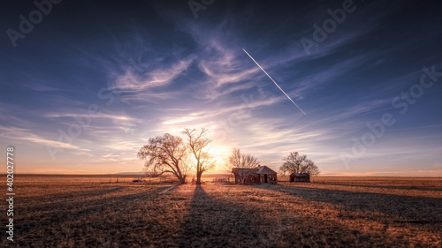 An old farmhouse on the eastern plains of Colorado in a rural setting at sunset. The sky is dramatic with wispy clouds. The old house if falling apart and abandoned. 