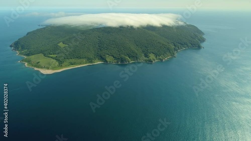 Aerial huperlapse epic seaside fog covered green island among blue sea ocean. Low white cloud over isle movement. Inspirational natural landscape Russia Far East. seascape. Rocky rugged shore tropical photo