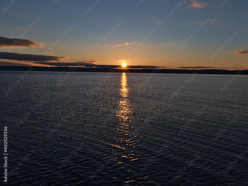 Beautiful sunset over calm Lake Constance viewed from town Meersburg, Germany with bright sun on horizon and reflections in the peaceful water in winter season with mostly clear sky and few clouds.