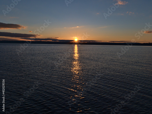 Beautiful sunset over calm Lake Constance viewed from town Meersburg  Germany with bright sun on horizon and reflections in the peaceful water in winter season with mostly clear sky and few clouds.