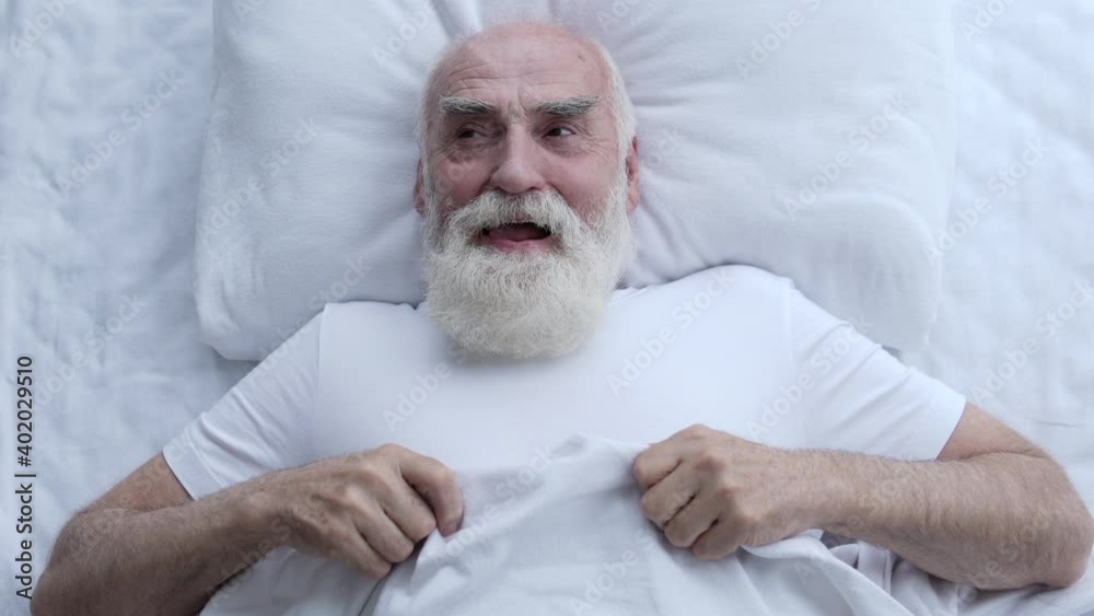 Cheerful greyhaired man lying in bed, feeling happy, thinking of funny moments Cheerful greyhaired man lying in bed, feeling happy, thinking of funny moments