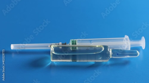 An ampoule with a vaccine and a syringe are on a blue background. The concept of vaccination against coronavirus.