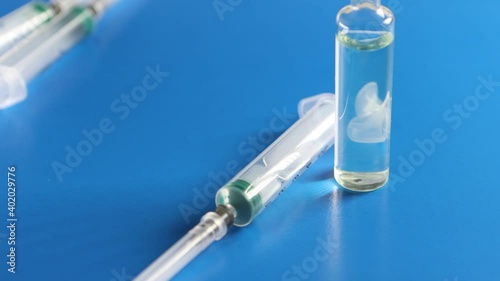 An ampoule with a vaccine and a syringe are on a blue background. The concept of vaccination against coronavirus.