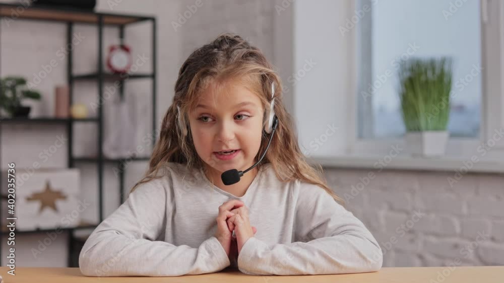 Happy cute little girl wears headset talking to web camera. Recording vlog, online video conference, video call, online education. Webcam view