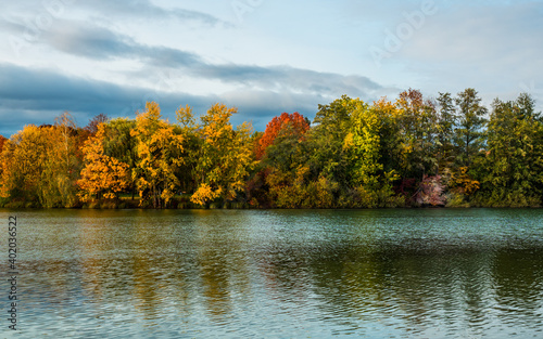 Autumn landscape at lake, multicolored trees, water mirror, sky clouds in background 