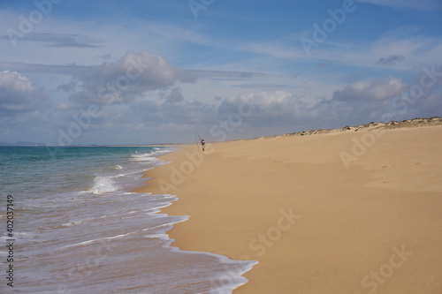 Fisherman fishing on a Comporta empty beach with ocean waves on the sand in Portugal