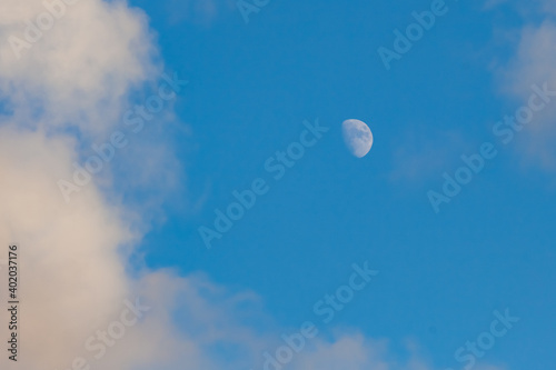 young moon on light blue sky, white clouds