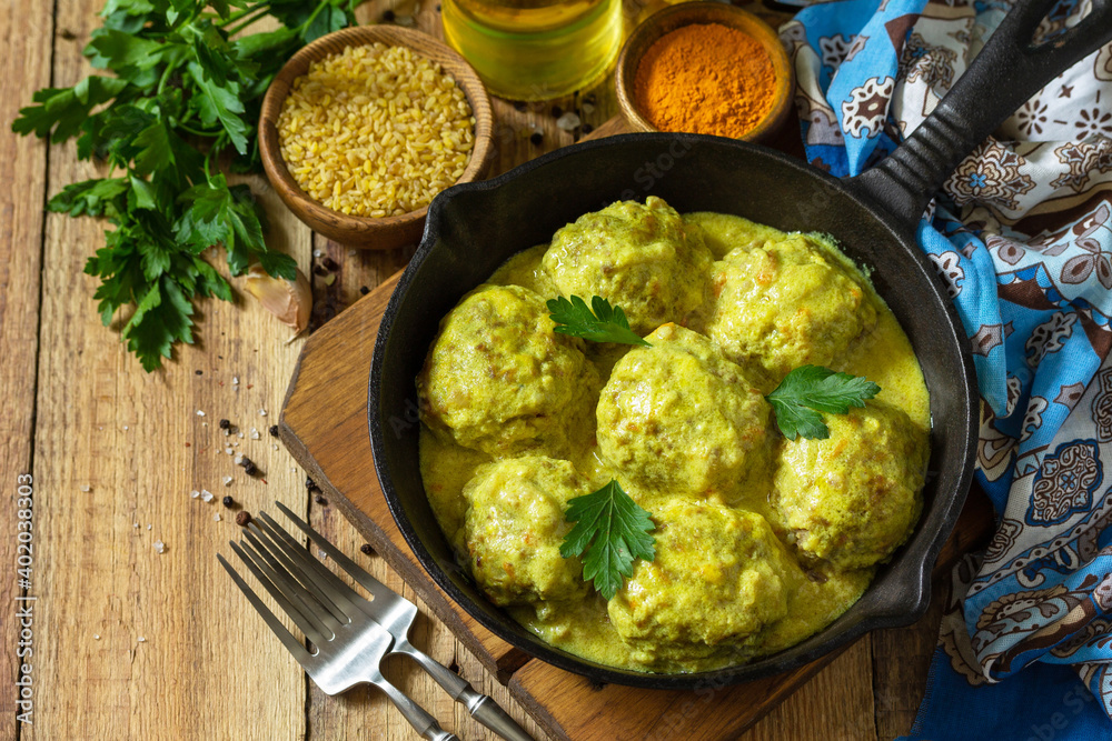 Meatballs with bulgur in sour cream and turmeric sauce in a cast-iron skillet on a rustic countertop. Copy space. Meatballs with bulgur in sour cream and turmeric sauce in a cast-iron skillet on a rustic countertop. Copy space.