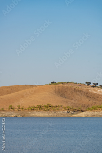 Desert like hill landscape with reflection on the water on a dam lake reservoir with blue sky in Terena, Portugal photo