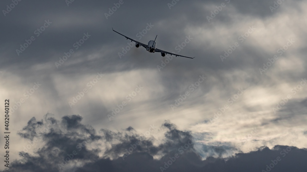 Fototapeta premium Unique dramatic dark gray clouds on dynamic cloudy sky background. The silhouette of airplane rising upward after takeoff. Storm weather conditions. Fast transportation, modern transport technology.