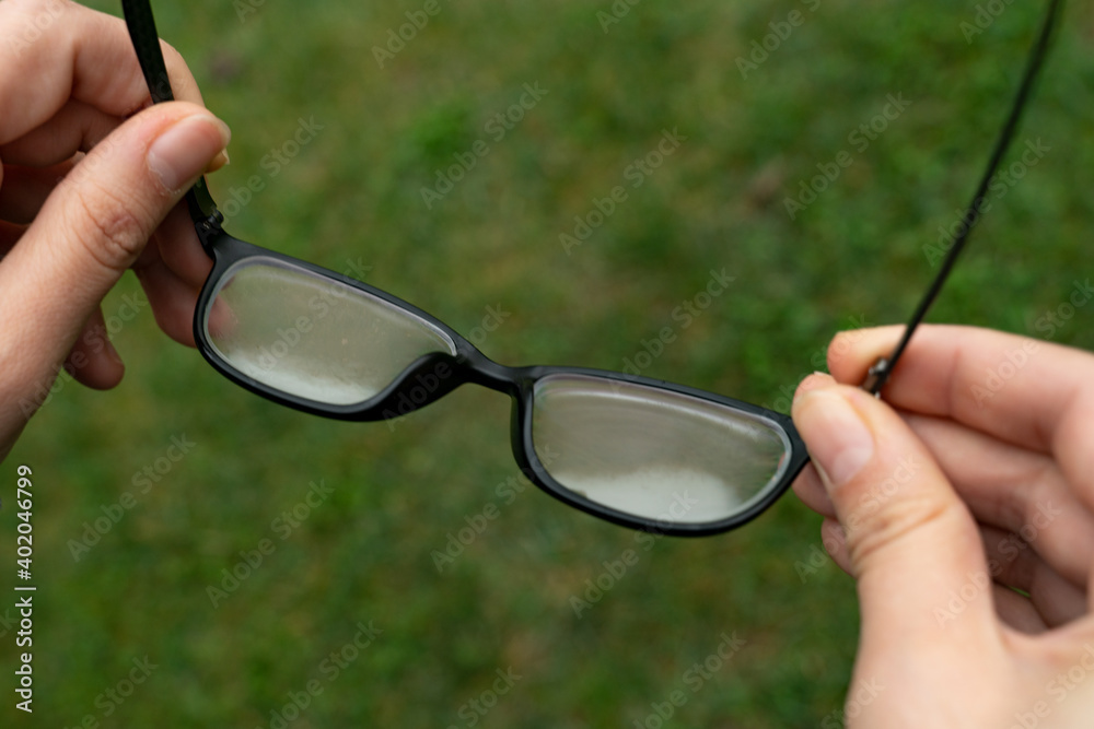 woman is holding her foggy glasses in hand to clean them during coronavirus  outbreak. glasses are fogged up because of warm breath. mask problems.  Stock Photo | Adobe Stock